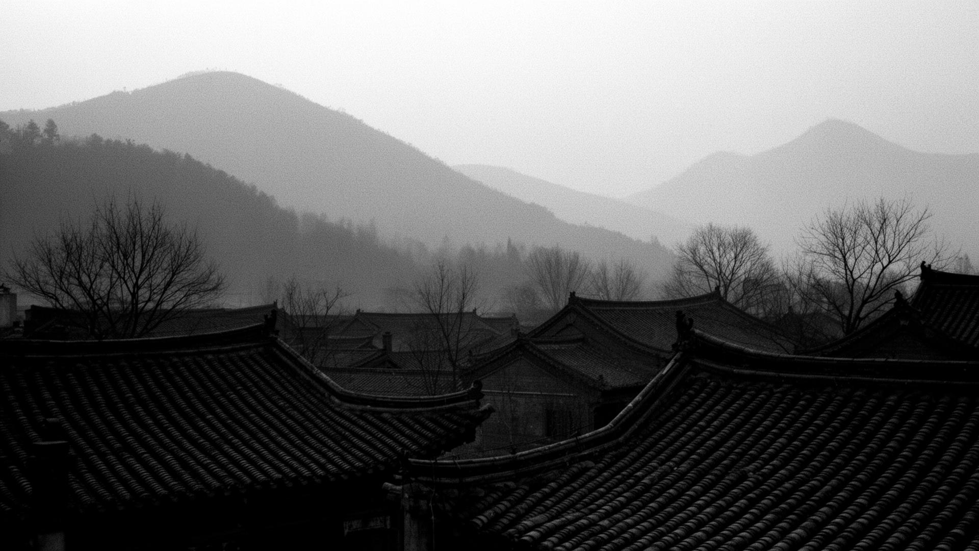 Misty layered mountains and tiled curved rooftops of a traditional Henan village at dawn.